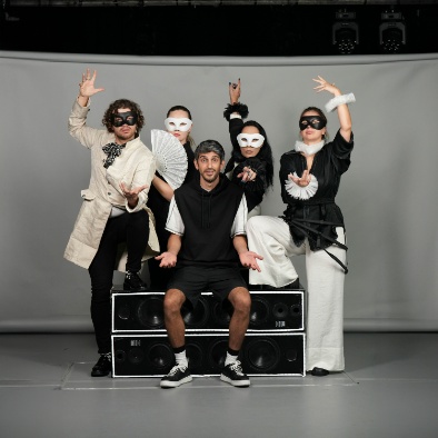 From the show "Something Is Missing". An actor is sitting confused while around him four other actors (three women and a man) are dressed-up and posing with their hands in the air. They are wearing eye masks.